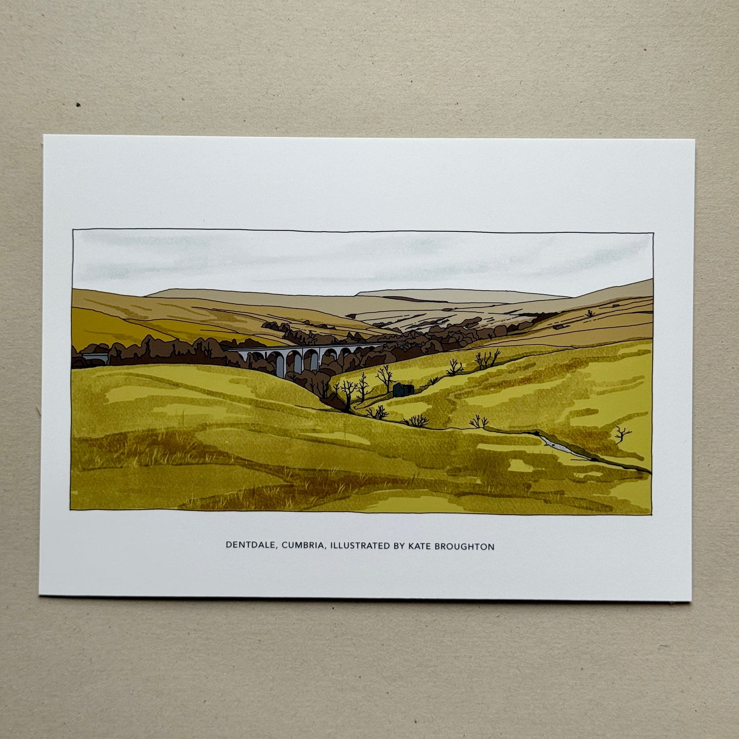 Art print of a landscape with a viaduct held by a hand on a beige background, Dental, Cumbria, by Kate Broughton