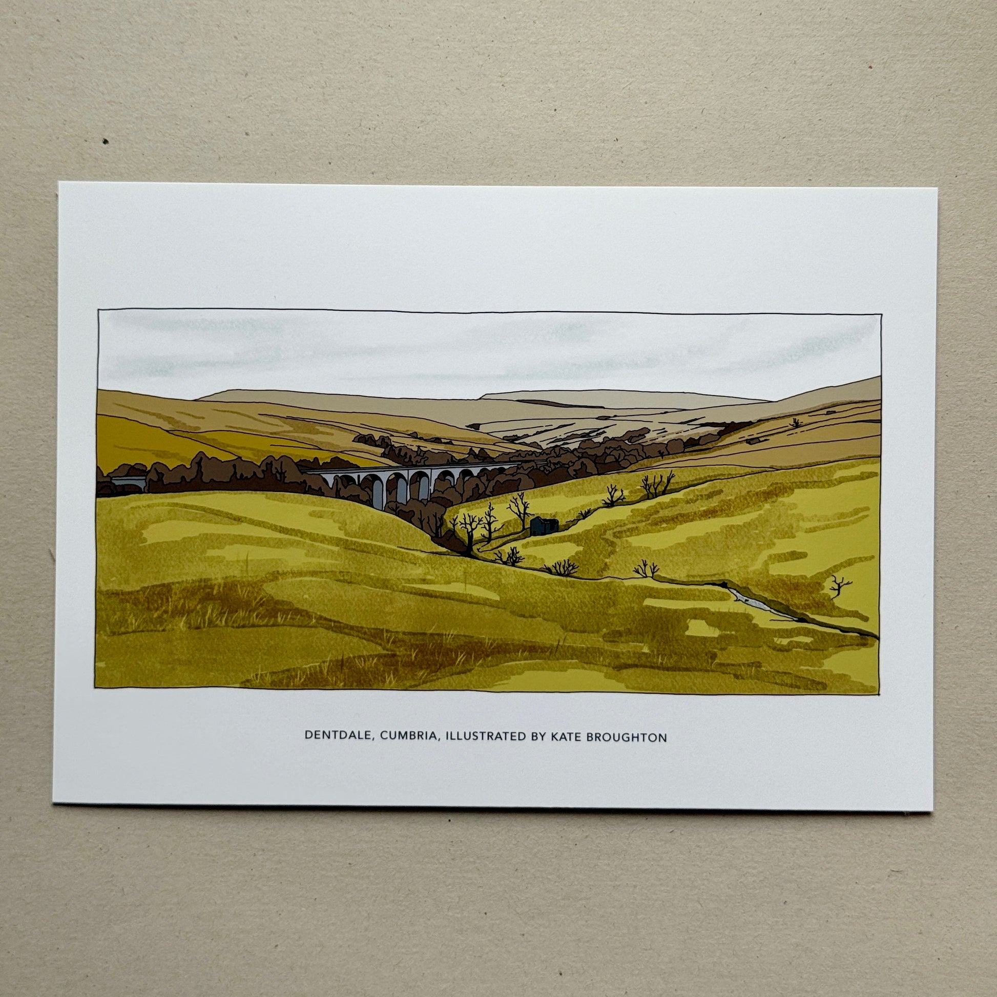 Art print of a landscape with a viaduct held by a hand on a beige background, Dental, Cumbria, by Kate Broughton