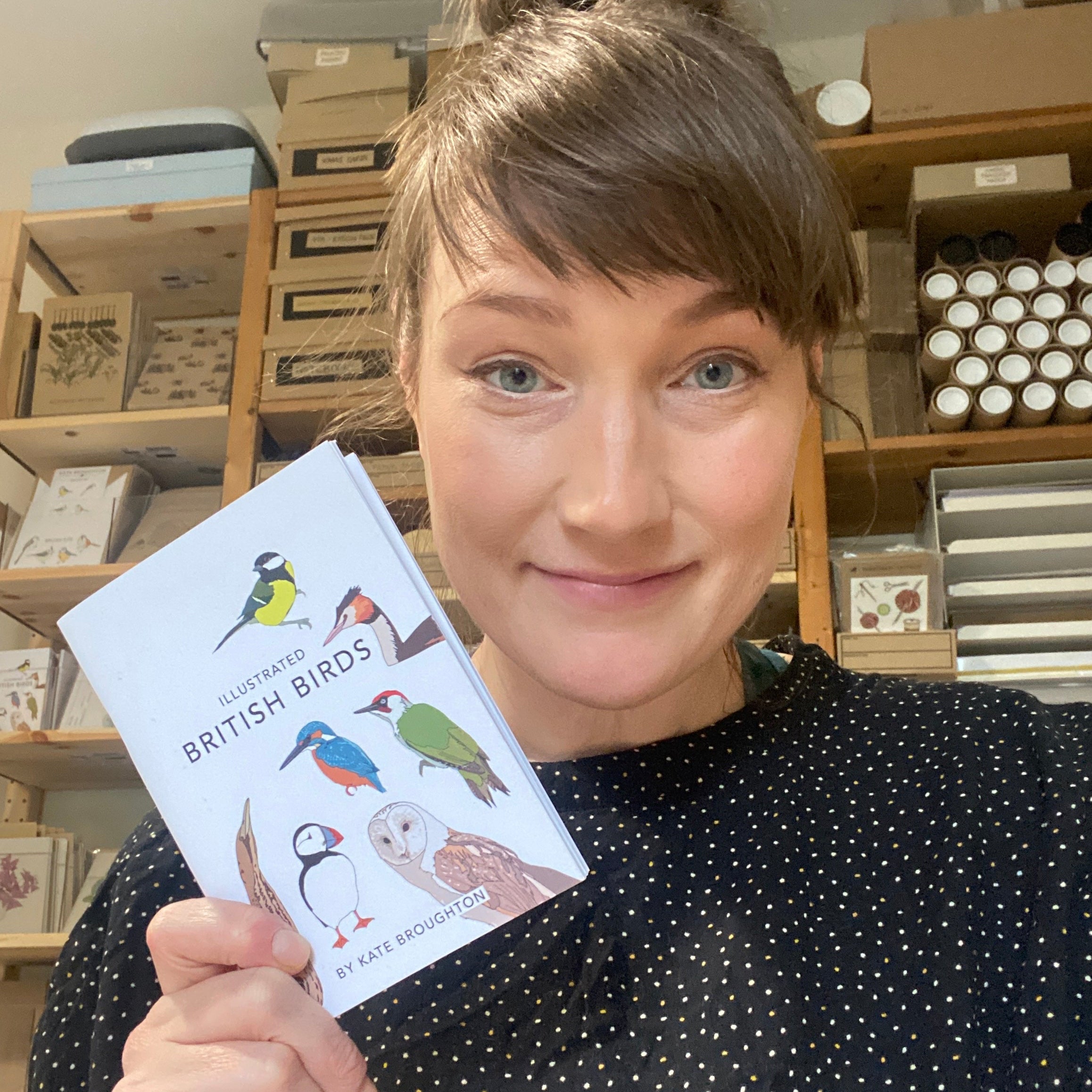 Artist Kate Broughton holding her book titled 'Illustrated British Birds' in her studio