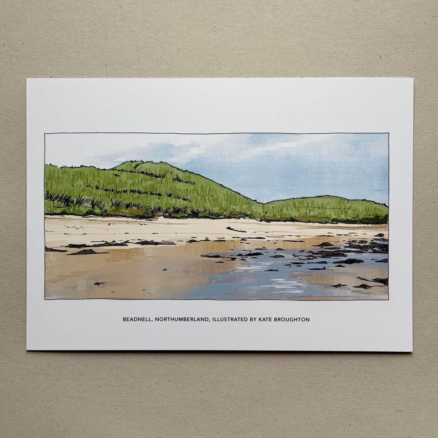 Print of a coastal landscape with green hills, sand dunes and a beach. Labelled Beadnell, Northumberland