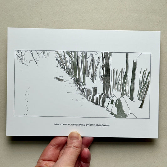 Hand holding a printed illustration of a snowy landscape with a path and trees. Otley, West Yorkshire, Chevin in snow