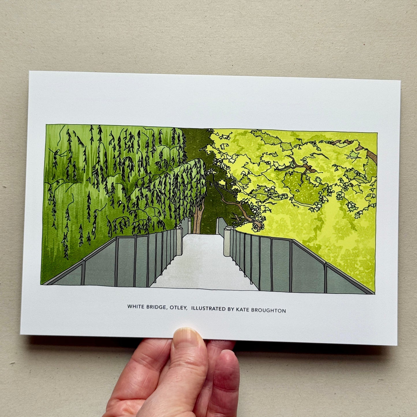 Hand holding a print with an illustration of the white bridge in Otley by Kate Broughton