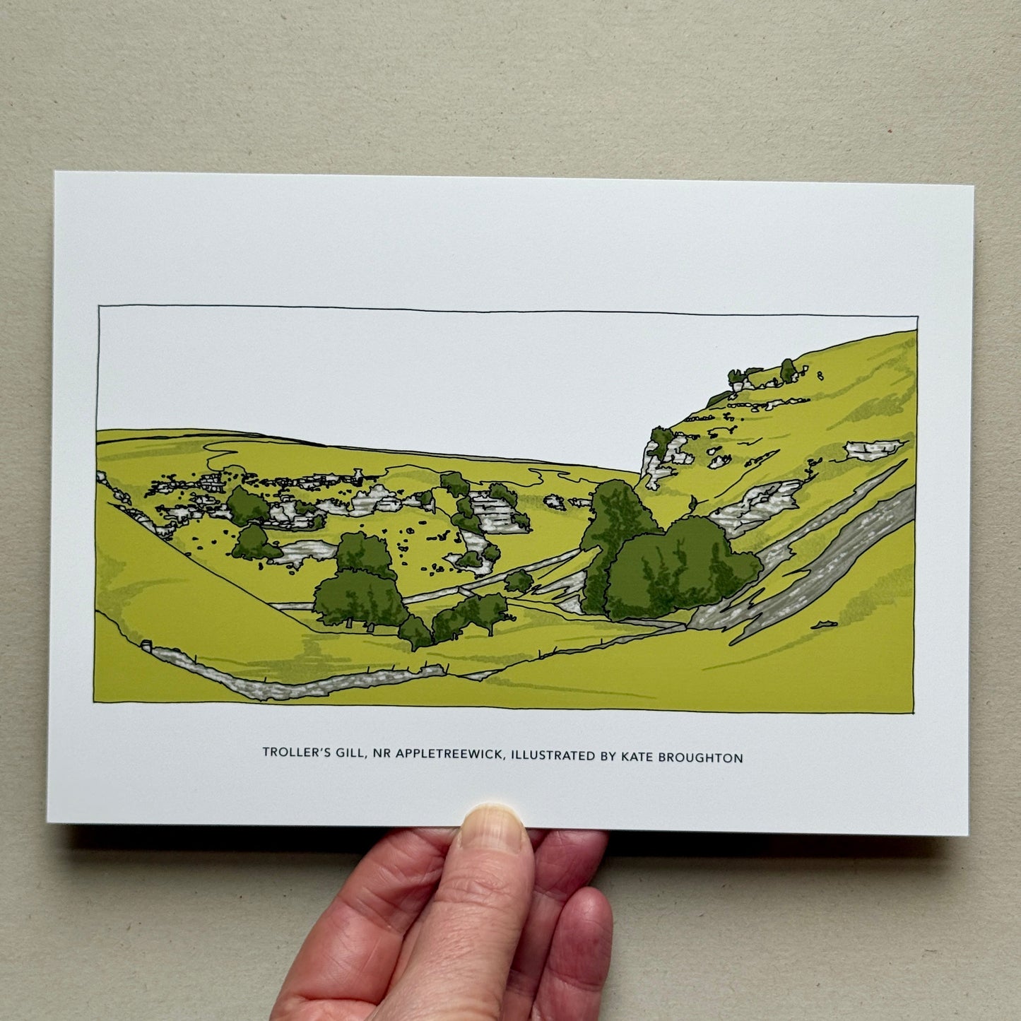 Hand holding Illustration of a landscape with greenery and dry stone walls. Labelled Troller's Gill, Nr Appletreewick, Yorkshire