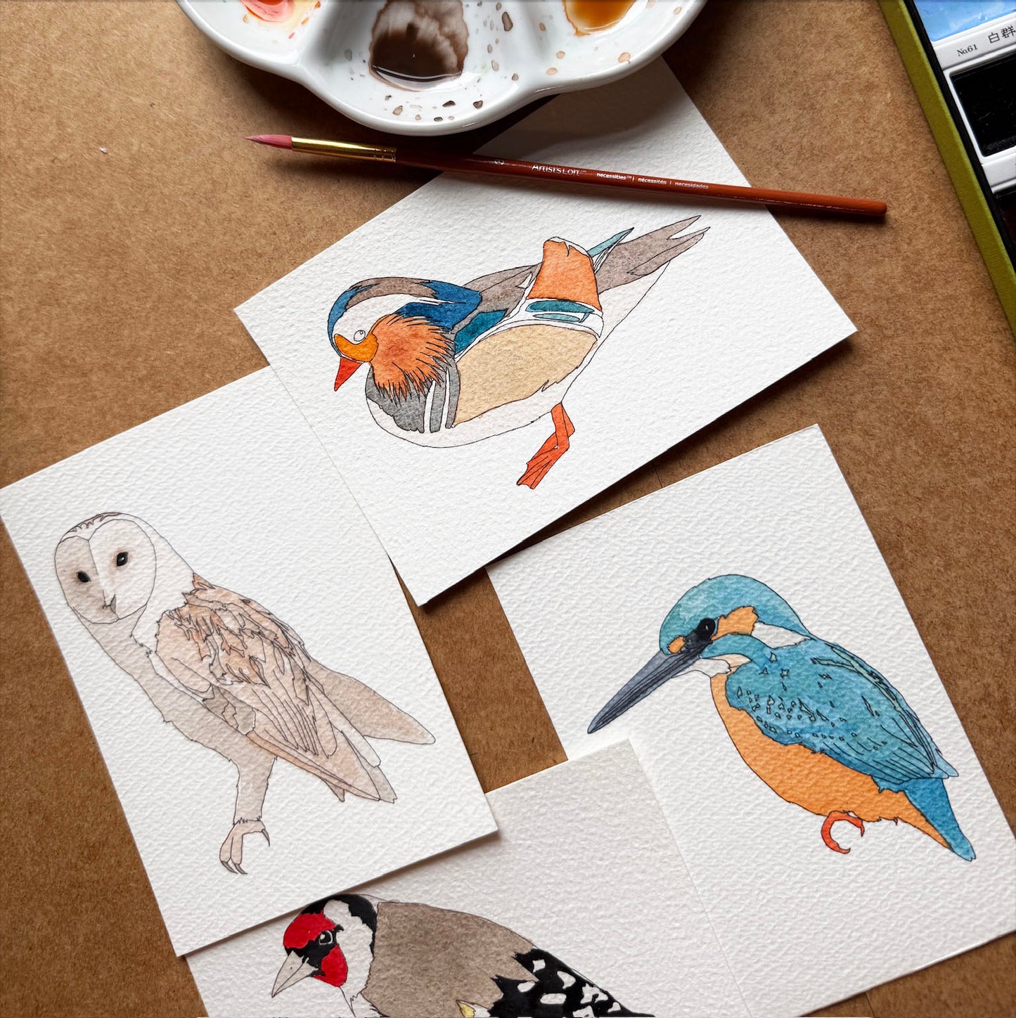 Illustrations of birds on paper with a paintbrush and cup in the background.