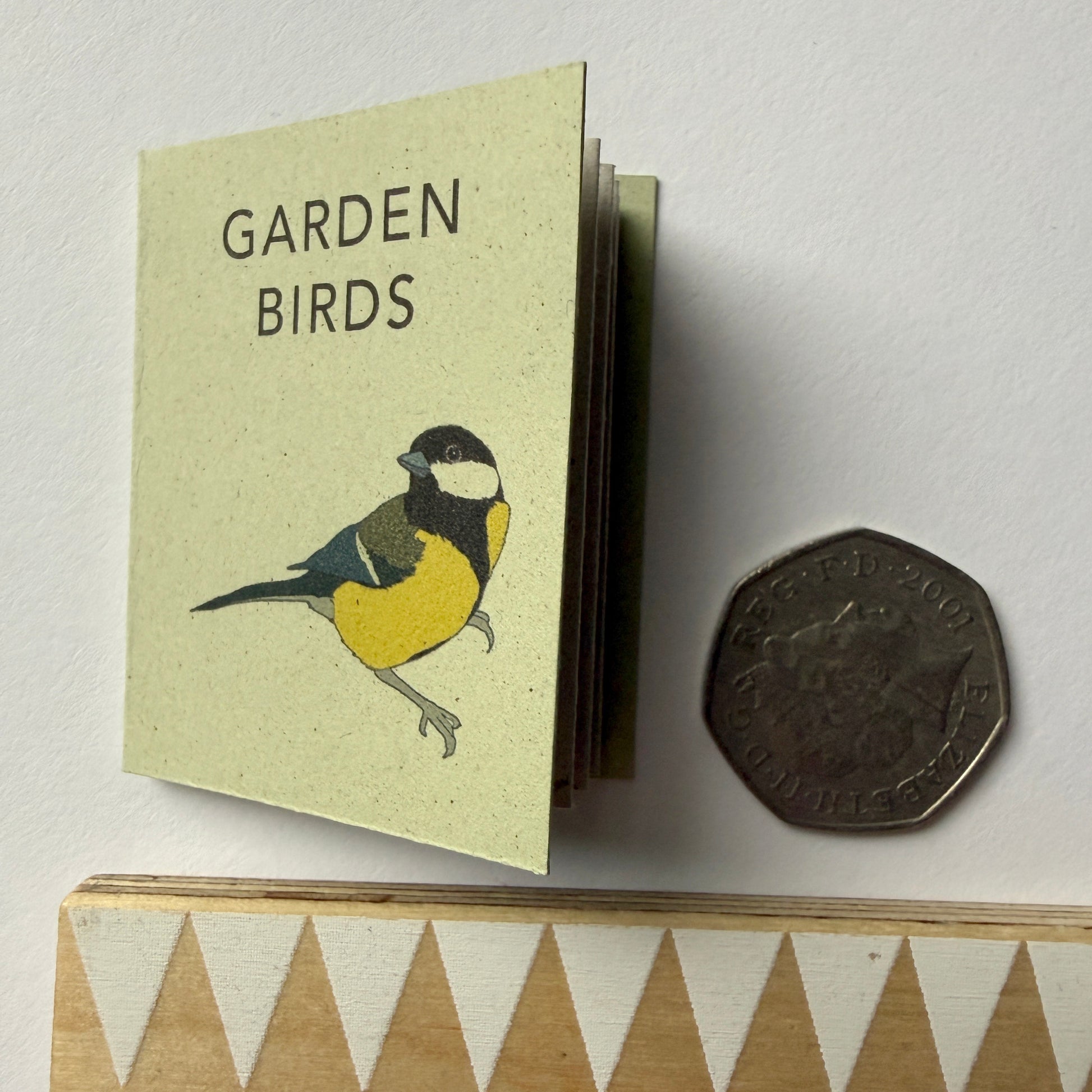 Miniature book titled 'Garden Birds' with a bird illustration, next to a coin for scale on a light background.
