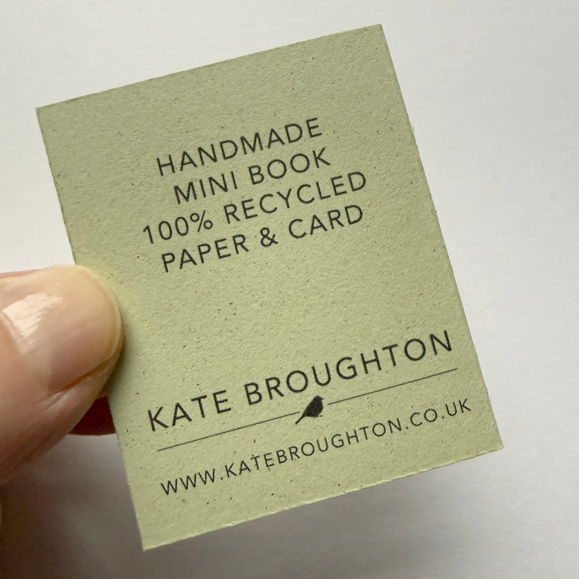Handmade mini book with recycled paper and card, held by a hand on a light background